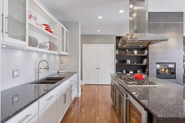 kitchen with beverage cooler, stainless steel gas cooktop, open shelves, island exhaust hood, and a sink