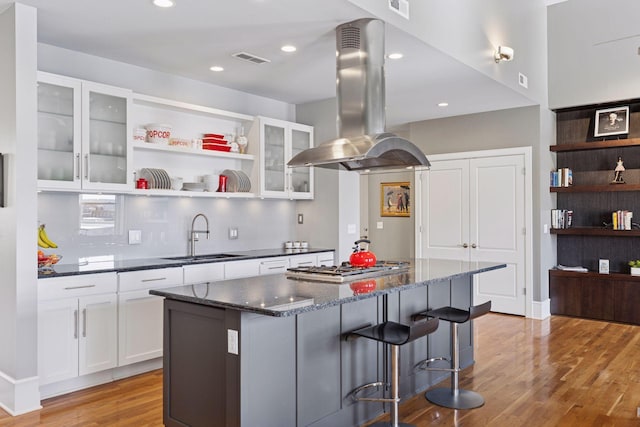 kitchen with island exhaust hood, a sink, a kitchen island, white cabinetry, and light wood finished floors