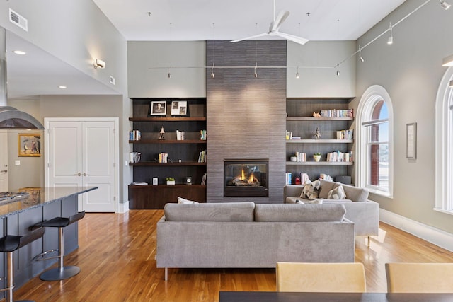 living room featuring visible vents, track lighting, a large fireplace, light wood-style flooring, and a towering ceiling