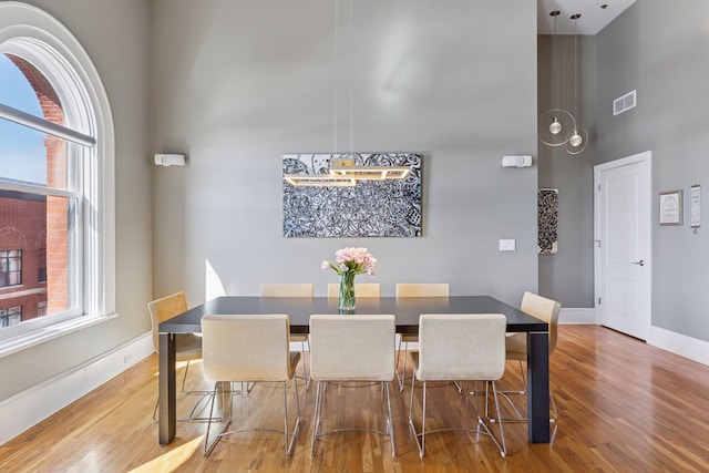 dining area featuring visible vents, a towering ceiling, baseboards, and wood finished floors