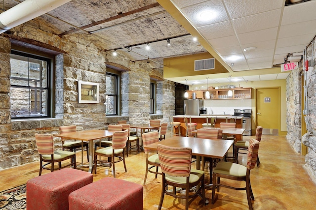 dining space featuring visible vents, rail lighting, concrete flooring, and a paneled ceiling