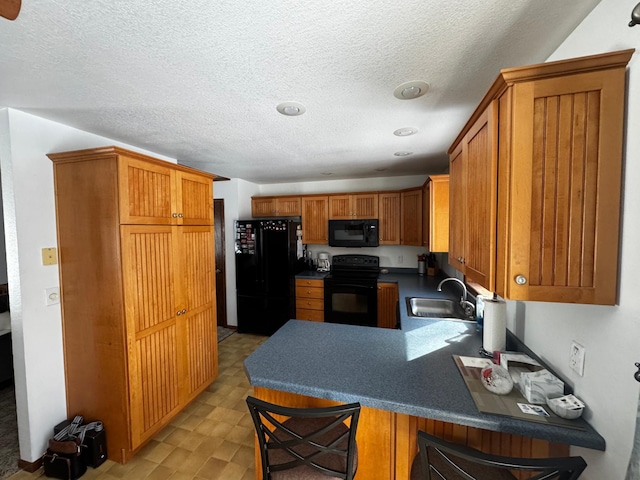 kitchen featuring a breakfast bar area, brown cabinets, a peninsula, black appliances, and a sink