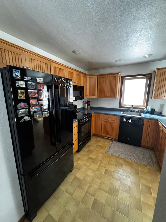 kitchen featuring dark countertops, light floors, a textured ceiling, black appliances, and a sink