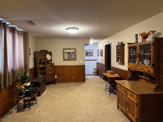 living area featuring visible vents, wainscoting, wood walls, light carpet, and a textured ceiling