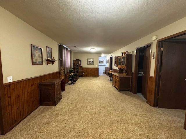 hallway with a wainscoted wall, a textured ceiling, light colored carpet, and wooden walls