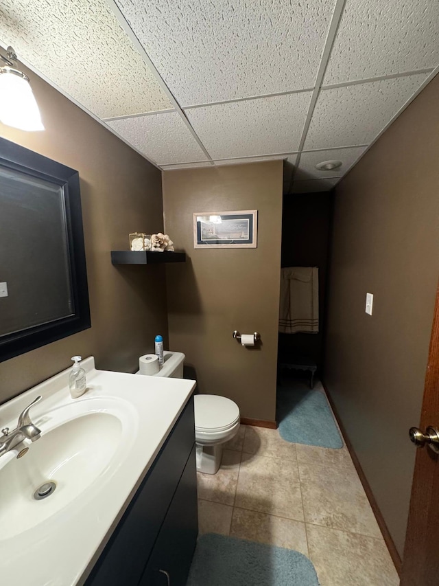 bathroom featuring a drop ceiling, tile patterned flooring, toilet, vanity, and baseboards