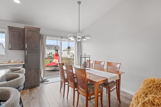 dining room featuring lofted ceiling, a notable chandelier, light wood-style flooring, and baseboards