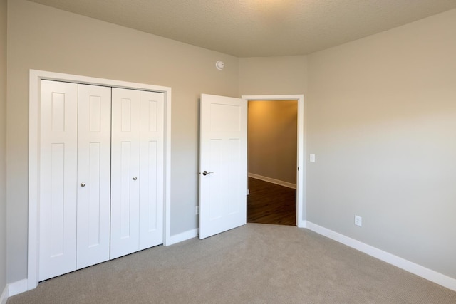 unfurnished bedroom featuring carpet floors, a textured ceiling, baseboards, and a closet