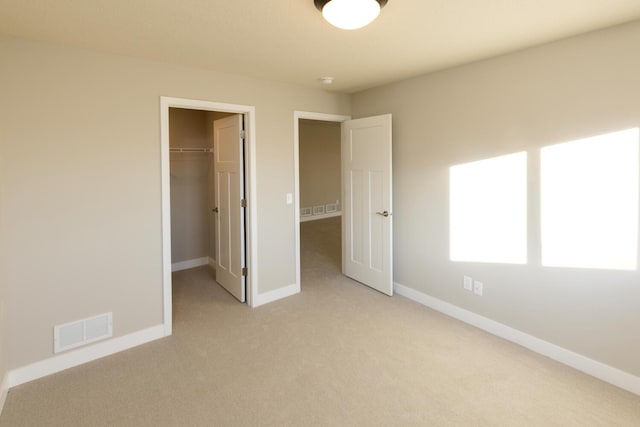 unfurnished bedroom featuring a spacious closet, light colored carpet, visible vents, and baseboards