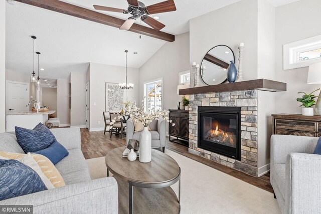 living room featuring high vaulted ceiling, a stone fireplace, wood finished floors, baseboards, and beam ceiling