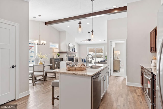 kitchen featuring light wood-style flooring, beamed ceiling, stainless steel appliances, a fireplace, and a sink