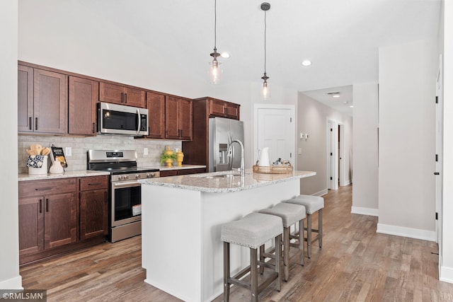 kitchen with tasteful backsplash, appliances with stainless steel finishes, a breakfast bar, and light wood-style flooring