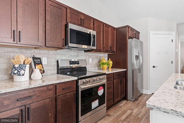 kitchen featuring light wood-style flooring, appliances with stainless steel finishes, light stone counters, vaulted ceiling, and backsplash