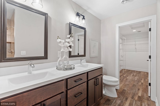 bathroom featuring toilet, double vanity, a sink, and wood finished floors