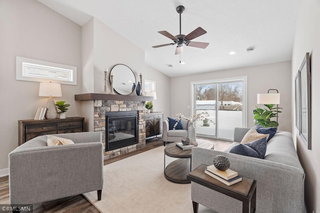 living room featuring baseboards, a ceiling fan, wood finished floors, vaulted ceiling, and a stone fireplace