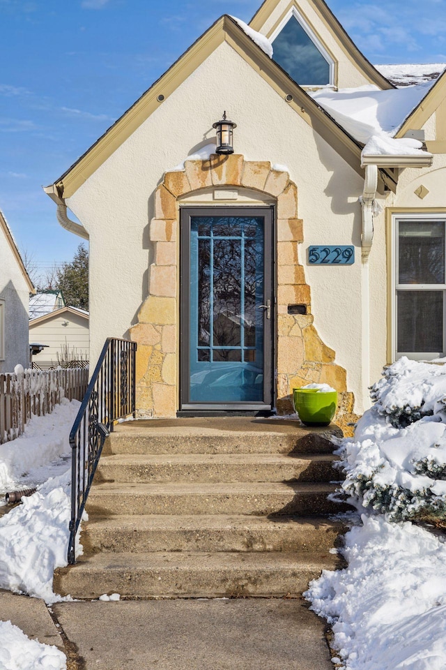 snow covered property entrance with fence and stucco siding