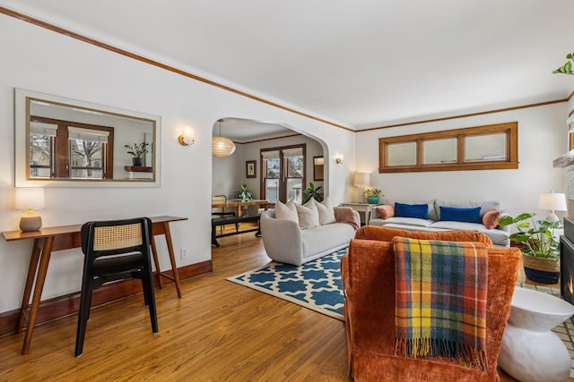 living area with ornamental molding, arched walkways, baseboards, and wood finished floors