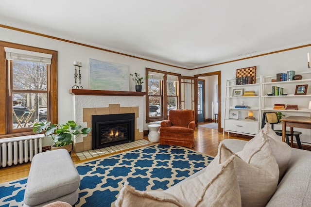 living area with radiator, crown molding, a tiled fireplace, and wood finished floors