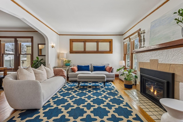 living area with ornamental molding, arched walkways, a fireplace, and wood finished floors