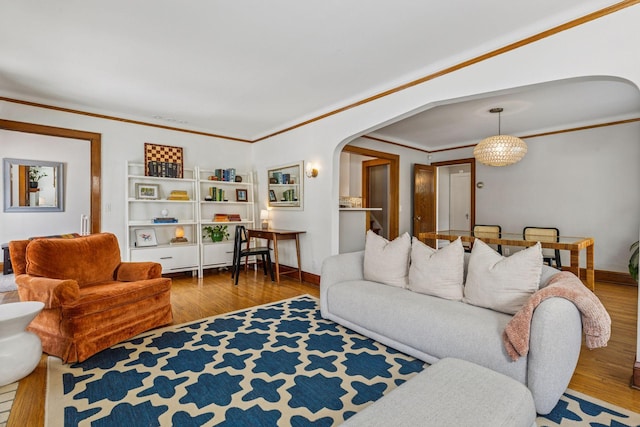 living area featuring arched walkways, baseboards, wood finished floors, and crown molding