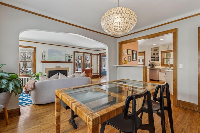 dining space featuring arched walkways, crown molding, plenty of natural light, and light wood-style floors