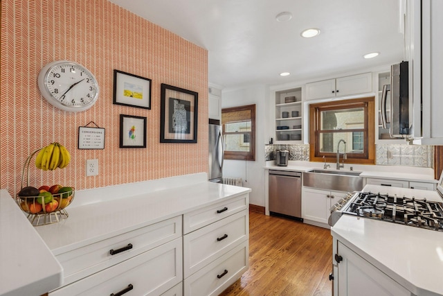 kitchen with stainless steel appliances, light countertops, white cabinets, a sink, and wallpapered walls