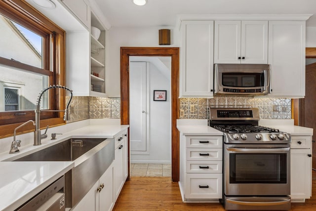 kitchen with tasteful backsplash, light countertops, appliances with stainless steel finishes, white cabinetry, and a sink