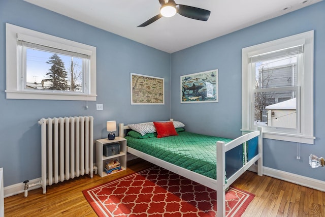 bedroom featuring ceiling fan, radiator heating unit, wood finished floors, and baseboards