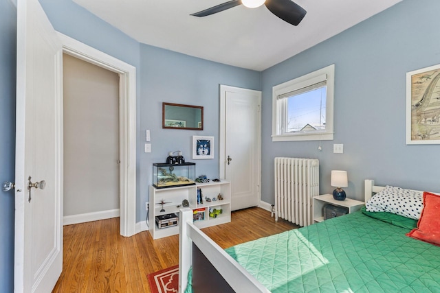 bedroom with a ceiling fan, radiator heating unit, baseboards, and wood finished floors