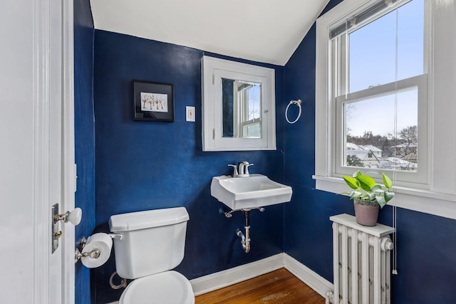 bathroom featuring toilet, wood finished floors, a sink, baseboards, and radiator