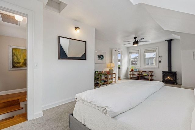 bedroom with a wood stove, carpet, baseboards, and ceiling fan