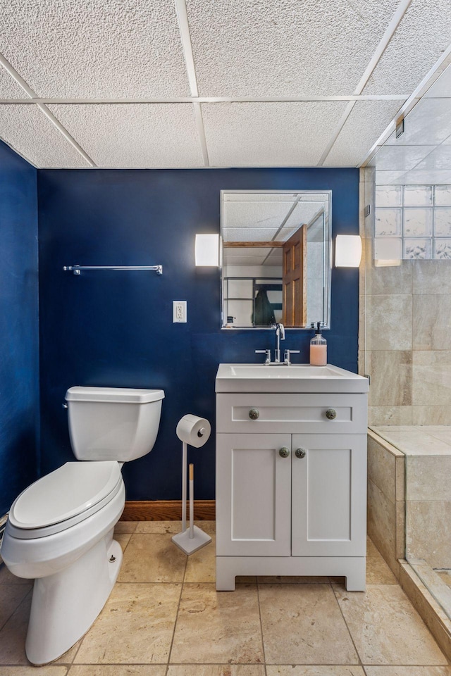 full bathroom with a paneled ceiling, toilet, vanity, baseboards, and tiled shower