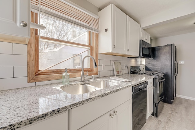 kitchen featuring white cabinets, a sink, light stone countertops, black appliances, and backsplash