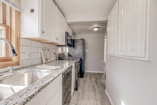 kitchen featuring baseboards, decorative backsplash, black appliances, white cabinetry, and a sink