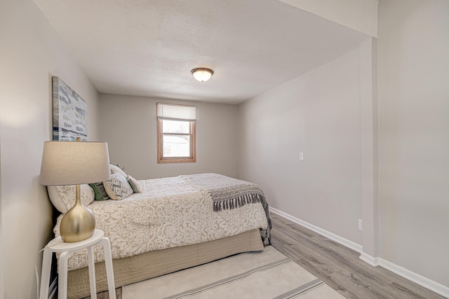 bedroom with a textured ceiling, baseboards, and wood finished floors