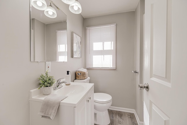 half bathroom featuring wood finished floors, vanity, toilet, and baseboards