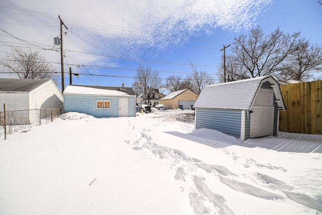 yard layered in snow with a shed, a detached garage, fence, and an outdoor structure