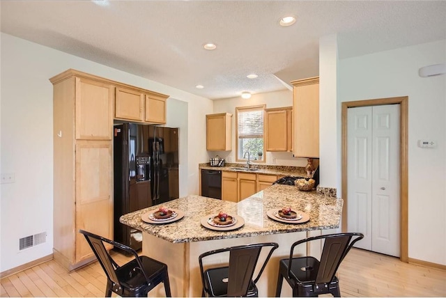 kitchen featuring light brown cabinets, visible vents, black appliances, a kitchen bar, and a sink