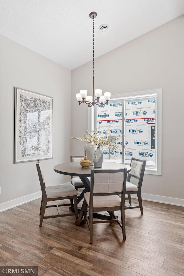 dining space with a notable chandelier, lofted ceiling, visible vents, wood finished floors, and baseboards