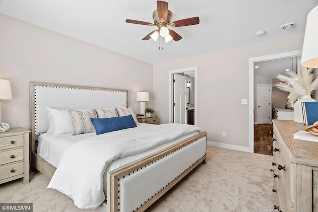 bedroom featuring baseboards, ensuite bathroom, a ceiling fan, and light colored carpet