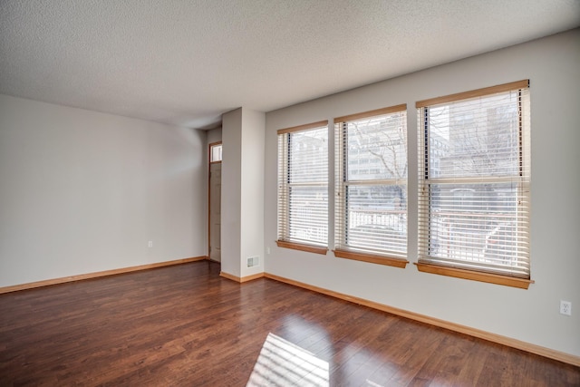 empty room with dark wood-style floors, visible vents, baseboards, and a textured ceiling