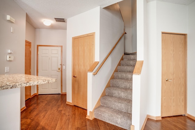 staircase featuring a textured ceiling, wood finished floors, visible vents, and baseboards