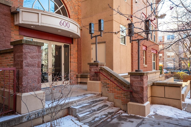 snow covered property entrance featuring french doors and brick siding