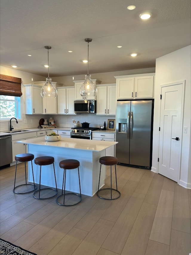 kitchen with light wood finished floors, a kitchen breakfast bar, a center island, stainless steel appliances, and a sink