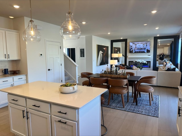 kitchen featuring a glass covered fireplace, open floor plan, a center island, white cabinetry, and backsplash