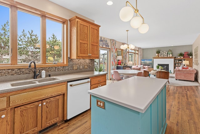 kitchen featuring white dishwasher, a sink, light wood finished floors, decorative light fixtures, and a kitchen island