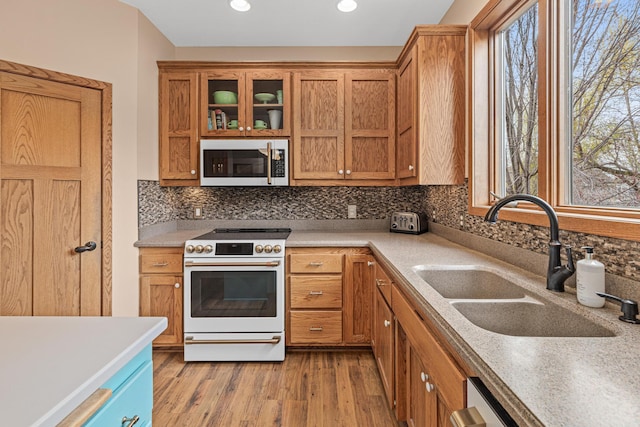 kitchen with a sink, light countertops, light wood-style flooring, electric stove, and decorative backsplash
