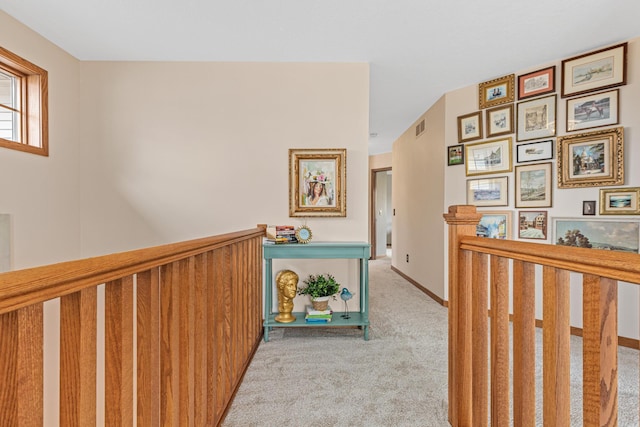 hall with carpet floors, baseboards, an upstairs landing, and visible vents
