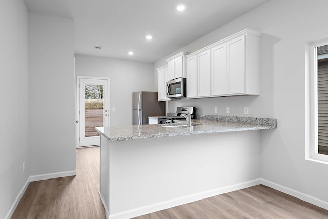 kitchen with appliances with stainless steel finishes, light wood-type flooring, baseboards, and light stone countertops