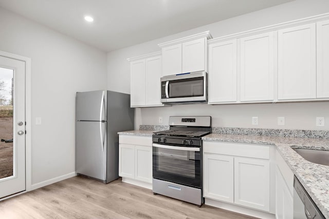 kitchen with recessed lighting, stainless steel appliances, white cabinets, light wood-type flooring, and light stone countertops